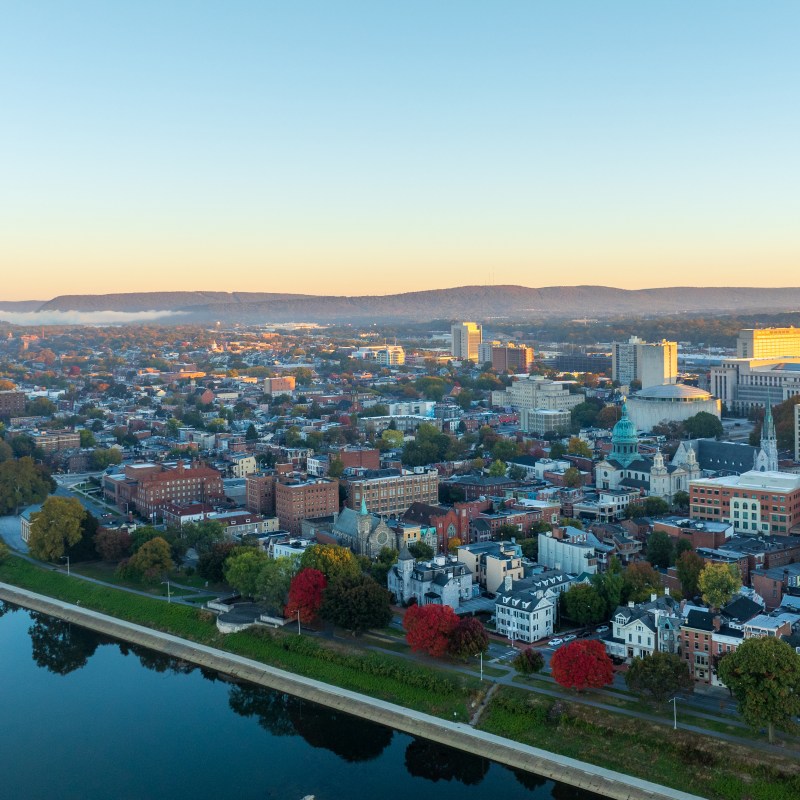 Aerial view of downtown Harrisburg, Pennsylvania, at sunrise, showcasing the city’s historic buildings, streets, and the Susquehanna River, with the landscape bathed in soft morning light.
